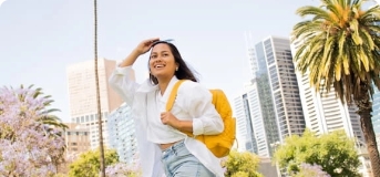 Happy woman with yellow backpack walking outside in area with palm trees.