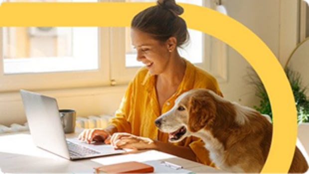 woman in yellow shirt using laptop with older dog by her side.