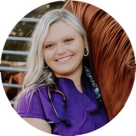 Penn Foster Vet Tech grad in purple scrubs with stethoscope posing with horse. 