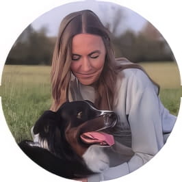 Penn Foster Vet Tech grad in light colored sweatshirt posing outdoors with brown and white dog. 